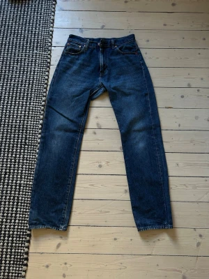  jeans från Levi's - Säljer ett par klassiska mörkblå jeans från Levi's med rak passform och fem fickor. Jeansen har en tidlös look med kontrastsömmar och läderpatch bak i midjan. Perfekta till en avslappnad stil och tillverkade i slitstark denim.