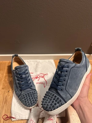 Loubotin Washed Blue - Säljer ett par blåa sneakers från Christian Louboutin i mocka med coola svarta nitar på tån. Skorna har vita sulor och matchande blå skosnören. Perfekta för dig som vill sticka ut med en edgy och lyxig stil. Size 44,5. 