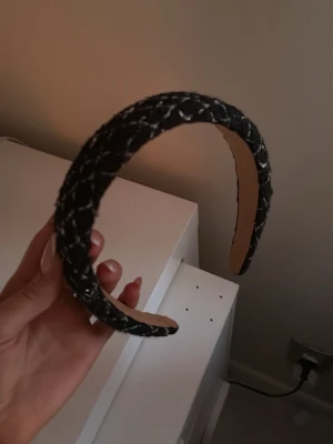 Svart tweeddiadem med vita detaljer - Snyggt svart diadem i tweed med vita sömmar som ger en trendig och lyxig känsla. Bred modell som sitter bekvämt på huvudet och ger en chic touch till din outfit. Perfekt accessoar för att lyfta din look.