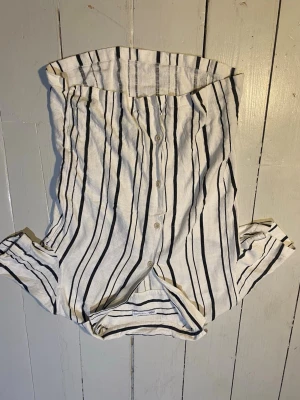 Randig linneskjorta från Zara - Säljer en snygg vit skjorta från Zara med svarta vertikala ränder. Skjortan har klassisk krage, knäppning framtill och är tillverkad i ett luftigt linnematerial. Perfekt för en avslappnad och trendig look.