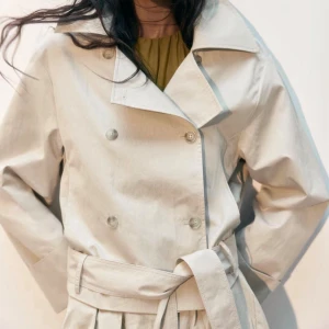 Beige trenchcoat med bälte - Säljer min trenchcoat från HM som aldrig använts, en Stilren beige trenchcoat med dubbelknäppning och brett slag. Jackan har ett matchande bälte i midjan och långa ärmar. Tillverkad i ett lätt bomullsmaterial som passar perfekt för övergångssäsonger. Enkel men trendig design som funkar till många looks. Nypris 500 kr, säljes pågrund av den ej kommer till användning.