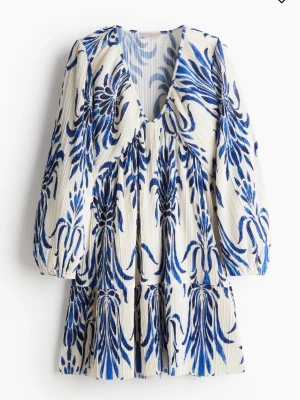 Vit och blå blommig klänning - Säljer en jättefin klänning med v-ringning och långa ärmar. Klänningen är vit med blått blommönster och har en avslappnad passform med volangdetaljer. Perfekt för sommarens alla tillfällen! Slutsåld på hm!