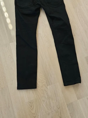 Svarta skinny jeans - Säljer ett par svarta skinny jeans med klassisk femficksdesign. Jeansen har smal passform och raka ben. Perfekta till en avslappnad streetstyle-look. Materialet känns mjukt och stretchigt för extra komfort.