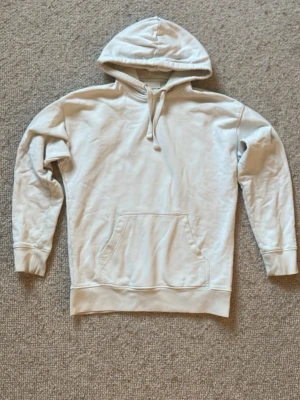 hoodie - En stilren ljusgrå hoodie med huva och dragsko. Hoodien har en stor magficka framtill och ribbade muddar vid ärmslut och nederkant. Perfekt för en avslappnad och bekväm look. Materialet ser ut att vara mjukt och skönt, troligen bomullsblandning.