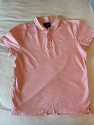 Rosa pikétröja från Bondelid - Snygg rosa pikétröja från Bondelid med klassisk krage och knappar framtill. Tröjan har korta ärmar och diskret broderad logga på bröstet. Tillverkad i mjuk bomull som känns skön mot huden. Perfekt för en avslappnad men ändå stilren look.