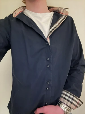 Mörkblp burburry skjorta  - Snygg mörkblå skjorta från burburry parfekt nu till sommaren🌞. Den är äkta och köpt i somras  från Nordiska kompaniet/NK storlek S sitter lite tajt den har knappar vid händerna så man kan vika ner om man vill det 👔. Skriv om det något ni undrar över 😊