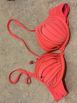 Korallrosa bikiniöverdel med veck - Snygg korallrosa bikiniöverdel med vadderade kupor och veckad design. Justerbara axelband och metallspänne bak. Perfekt för strandhäng eller poolparty. Den är inte svart det är ljuset 