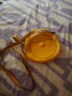 Axelremsväska senapsgul - Säljer denna väskan i senapsgul. Står att märket är STR (se bild) och är förmodligen köpt på någon turistbutik i spanien, grekland, italien osv. Troligtvis köpt i Ibiza eller Mallorca.