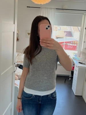 Grå stickad tröja med kort ärm - Säljer en grå stickad t-shirt med korta ärmar och rund hals. Den är lite mindre i storleken så den passar om man brukar ha storlek xxs-s. 💕