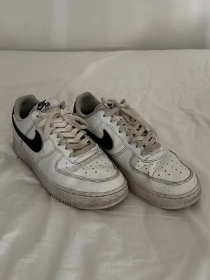 Nike Air Force 1 vita sneakers - Säljer nu mina skor eftersom de har blivit för små. Vita skor med svarta detaljer. Storlek 44,5 (28,5 cm).  Lite slitna på insidan, se bild 7. Skorna har veck (creased), men det blir alla skor med tiden.