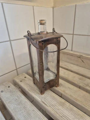 Vintage lykta i glas och metall - Unik vintage lykta med fyrkantig form, tillverkad i glas och metall med kopparfärgad finish. Har ett handtag i metall för enkel upphängning eller bärande. Passar perfekt som dekoration eller mysbelysning.