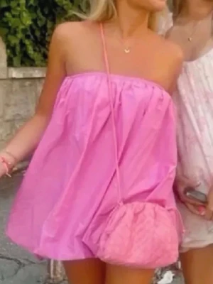 Rosa axelbandslös kortklänning - Säljer en söt rosa kortklänning med axelbandslös design och luftig passform. Klänningen har en ballongliknande form och är perfekt för varma dagar. Tillverkad i ett lätt material som ger en avslappnad och trendig look.