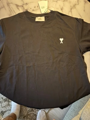 Svart vit loga ami paris tshirt S/M - Säljer en stilren beige tshirt från Ami. Helt ny med tags, säljer pga ingen användning samt rensar garderob. Modellen har ett tjockt material perfekt för sommarkvällar. Storlek S/M. Ny pris: 1099-1300. Mitt pris: 549 eftersom jag vill rensa snabbt garderoben