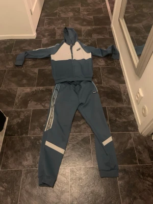 Blå mjukisbyxor från Mackenzie - Säljer ett par blå mjukisbyxor från Mackenzie med vita detaljer och logga på benet. Byxorna har resår i midjan med dragsko och muddar vid bensluten. Snygg sportig look med sidoremsa och bekväm passform.