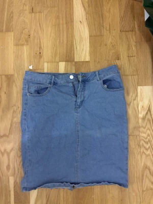 Blå jeanskjol från Vero Moda - Säljer en klassisk blå jeanskjol från Vero Moda i storlek XL. Kjolen har fem fickor, knapp och dragkedja framtill samt rå kant nedtill för en avslappnad look. 