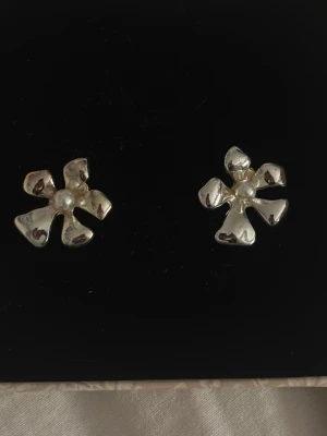 Blommiga örhängen med pärldetalj - Snygga örhängen i form av blommor i silvrig metall med en liten pärla i mitten. Perfekta för att ge din look en unik och trendig touch. 