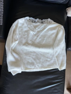 Vit stickad tröja med spets från H&M - Supersöt vit stickad tröja från H&M med v-ringning och dekorativ spetskant runt halsen. Tröjan har lång ärm och är gjord i ett mjukt, fluffigt material som känns riktigt mysigt. Perfekt för dig som gillar en romantisk och trendig look.
