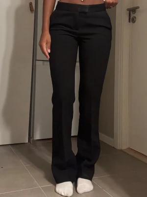 Svarta kostymbyxor med raka ben - Snygga svarta kostymbyxor med low midja och raka ben. Byxorna har en klassisk passform och stilren look, perfekta till en trendig outfit. Materialet ser ut att vara en mjuk och följsam mix, vilket ger en skön känsla och bra fall.
