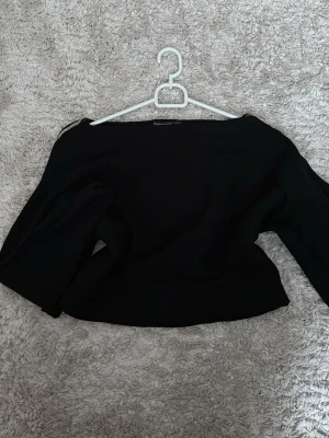 Svart ”offshoulder” topp - Säljer en svart ”offshoulder” (den är inte riktigt offshoulder) topp från Stradivarius i storlek XS. Toppen har en croppad passform och är ribbad i materialet vilket ger en snygg struktur.