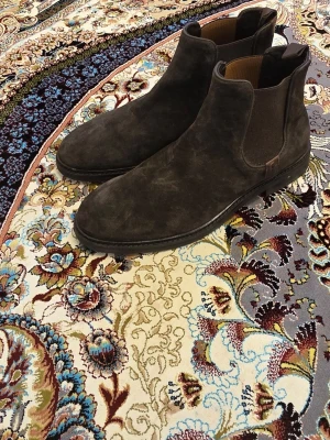 Mörkbruna Chelsea boots i mocka - Säljer ett par stilrena mörkbruna Chelsea boots i mjuk mocka. Klassisk siluett med elastiska resårpaneler på sidorna och låg klack. Perfekta för dig som vill ha en tidlös och snygg look till hösten eller vintern.