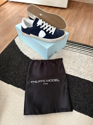 Philippe Model blåvita sneakers - Snygga sneakers från Philippe Model i blått och vitt med klassisk låg siluett. Ovandel i mocka och läder, vita skosnören och gummisula. Kommer med originalpåse och låda. Perfekta för dig som gillar stilrena och trendiga skor. Dm vid intresse