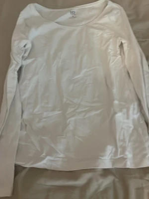 Vit långärmad topp i bomull - En basic vit långärmad topp med rund halsringning. Tillverkad i mjuk bomull, perfekt att styla lager på lager eller bära som den är. Enkel och clean design som passar till allt.