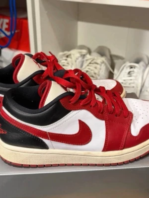 Nike Air Jordan 1 Low Chicago - Säljer ett par Nike Air Jordan 1 Low Chicago med klassisk färgkombination i rött, vitt och svart. Skorna har röd swoosh, röda snören och detaljer, samt svart häl och krage. Ovandelen är i läder och yttersulan är röd. Perfekta sneakers för dig som gillar streetstyle.