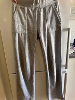 Grå mjukisbyxor Juicy Couture - Säljer ett par grå mjukisbyxor från Juicy Couture med raka ben, bred resårmidja och dragsko. Byxorna har två stora fickor fram och en diskret broderad Juicy-logga på ena fickan. Perfekta för chill dagar eller när du vill vara extra bekväm. 