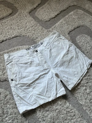 Vita shorts från Sail Racing - Snygga vita shorts från Sail Racing med klassisk passform. Shortsen har dragkedja, knappstängning och bälteshällor. Tillverkade i bomull för en skön känsla. Perfekta för varma dagar och enkel att matcha med olika stilar.