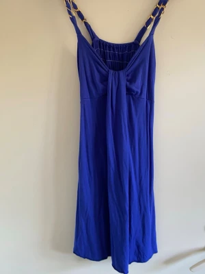 Royalblå sommarklänning med gulddetaljer 💙✨ - Jättefin kornblå/royalblå klänning köpt utomlands som ger en lyxig Y2K-vibe! Gjord i en mjuk och stretchig bomullskvalitet som sitter fantastiskt bekvämt på.📌 Storlek & Passform:Storlek: Saknar storlekslapp men uppskattas som en solid M.Flexibel passform: Tack vare stretch i tyget och en bred smock (resår) i ryggen passar den allt från en storlek S till en mindre L beroende på önskad passform.Mått: Längd ca 92 cm (mätt från axelband). Armhåla till armhåla ca 37 cm osträckt (går att töja ut mycke