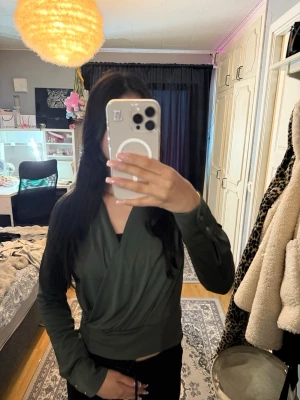 Mörkgrön tröja - Snygg mörkgrön tröja med knappar vid ärmsluten. Toppen har en smickrande omlottdesign och sitter tajt i midjan. Perfekt att styla med både jeans och kjol för en trendig look.