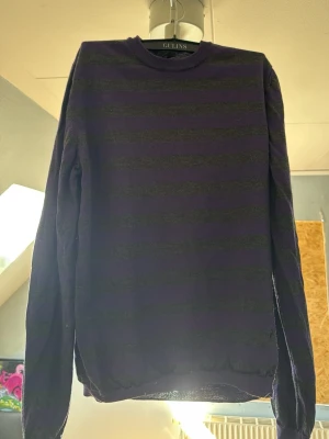 Randig lila stickad tröja Hugo Boss - Stickad tröja från Hugo Boss i slim fit-modell. Tröjan har lila och mörkgrå horisontella ränder, rund halsringning och långa ärmar. Perfekt för dig som gillar stilrena och klassiska plagg med en twist.