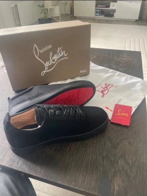 Svarta sneakers från Christian Louboutin - Snygga svarta sneakers från Christian Louboutin med klassisk röd sula. Skorna har en stilren design i mocka och läder, svarta skosnören och diskreta detaljer. Perfekta för dig som vill ha något exklusivt och trendigt i garderoben.