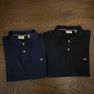 Paketpris! 2 st långärmade GANT pikétröjor (Marinblå & Svart) – Storlek 2XL - Klassisk mörkblå pikétröja från Gant med lång ärm och krage. Tröjan har två knappar framtill och diskret broderad logga på bröstet. Perfekt för en stilren och avslappnad look. Pris kan diskuteras 
