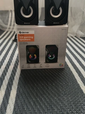 Denver 2.0 gaminghögtalare RGB - Säljer ett par svarta Denver 2.0 gaminghögtalare med RGB-belysning. Högtalarna har en modern, kantig design med färgade ljuseffekter, volymkontroll och USB-ström. Perfekta för gaming och musik, ansluts via 140 cm AUX-kabel.