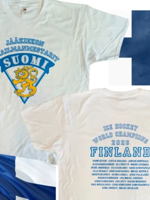 World Champions 2026 | Finland | Suomi tröja - Vit t-shirt från Fruit of the Loom med blå och gul Suomi-logga och lejon på framsidan samt texten 'Jääkiekon Maailmanmestarit'. Baksidan har tryck med 'Ice Hockey World Champions 2026 Finland' och guldmedaljörer as spelarnamn. Storlek Medium