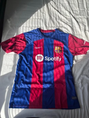 FC Barcelona matchtröja Nike - Säljer en officiell FC Barcelona matchtröja från Nike med breda blå och vinröda ränder. Tröjan har klubbmärke, Nike-logga och Spotify som sponsor framtill samt UNHCR-logga bak. Tillverkad i lätt och ventilerande material, perfekt för fotboll eller träning.