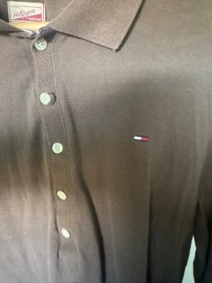 Brun långärmad skjorta Tommy Hilfiger - Snygg brun långärmad skjorta från Tommy Hilfiger Denim med klassisk krage och knappar framtill. Liten broderad logga på bröstet. Perfekt för en stilren och avslappnad look. Storlek osäker men jag tror S eller M