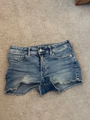 Jeansshorts med en fjäril på fickan strl 152 från H&M - Säljer ett par blå jeansshorts med en fjäril på fickan. Det är i bra skick men har används mycket.  De är från H&M i strl 152. De passar perfekt nu till sommaren.