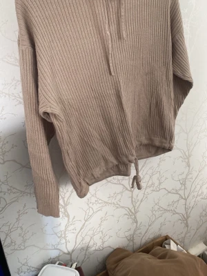 Beige ribbad tröja med dragsko - Säljer en beige ribbad tröja med långa ärmar och dragsko i nederkanten. Tröjan har en halv dragkedja framtill och är tillverkad i ett mjukt, stretchigt material. Perfekt för en avslappnad och trendig look.