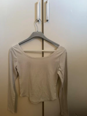Vit långärmad topp med rund hals - En enkel och stilren vit långärmad topp med rundad halsringning. Toppen har en tight passform och är tillverkad i mjukt bomullsmaterial, perfekt att matcha med jeans eller kjol för en clean look.