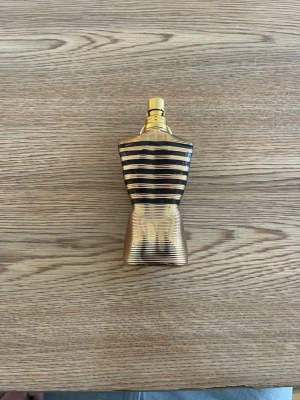 Jean Paul Gaultier Le Male Parfym - Säljer en ikonisk parfym från Jean Paul Gaultier i form av en guldig torso med svarta ränder. Flaskan har en unik design som sticker ut och är tillverkad i metall och glas. Perfekt för dig som gillar snygga och annorlunda parfymflaskor.