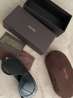 Svarta solglasögon från Tom Ford - Snygga svarta solglasögon från Tom Ford med bred båge och klassisk design. Glasögonen har guldfärgade detaljer vid skalmarna och kommer med originalfodral, putsduk och box. Perfekta för dig som vill ha en exklusiv accessoar hör av er vid frågor vet ja :)