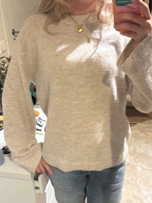 Beige stickad tröja i oversize - Mysig beige stickad tröja med avslappnad passform och långa ärmar. Tröjan har rund halsringning och ribbade muddar vid ärmslut och nederkant. Perfekt att matcha med jeans för en enkel och stilren look. Helt oanvänd från Gina tricot young 