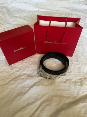 Svart skärp från Salvatore Ferragamo - Stilrent svart skärp från Salvatore Ferragamo med ikoniskt silverfärgat spänne i metall. Skärpet är gjort i skinn och levereras med originalförpackning och påse. Perfekt accessoar för att lyfta din outfit.