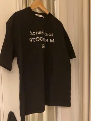 Acne Studios T-shirt  - Svart t-shirt från Acne Studios med ikoniskt tryck “Stockholm 1996”. Riktig clean & minimalist vibe – passar till ALLT. Oversized fit som sitter fett snyggt både casual och street.  Original, bra skick och sjukt lätt att styla med jeans, cargo eller hoodie över. Acne går aldrig ur stil 💯 Perfekt om du vill ha en dyr look utan att betala nypris. Skriv vid frågor 