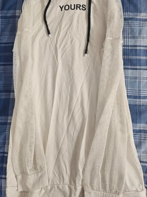 Vit hoodie med meshärmar och text - Snygg vit hoodie från YOURS med svarta dragsnören och texten 'YOURS' på bröstet. Ärmarna är i meshmaterial som ger en cool och sportig vibe. Perfekt för dig som vill sticka ut lite extra. Mjuk bomullskänsla i tyget.