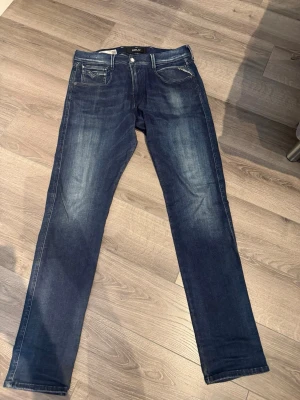 Mörkblå Replay jeans med raka ben - Säljer ett par mörkblå jeans från Replay med raka ben och snygga slitningar framtill och baktill. Klassisk femficksmodell med Replay-lapp bak i midjan. Jeansen är tillverkade i denim och har kontrastsömmar för en cool look. Säljer ändast för 500, men pris kan diskuterar vid snabb affär 