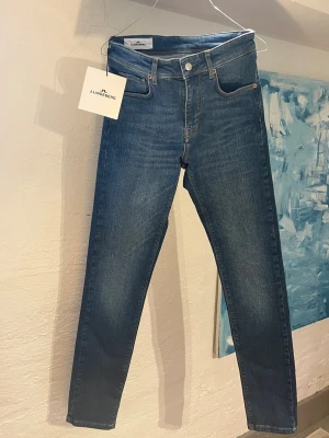 Blå jeans från J.Lindeberg - Helt nya jeans från J.Lindeberg. Storlek 28/32 i modellen Damien. Jeansen har en brun läderpatch bak i midjan och diskret logga på myntfickan, med en otrolig tvätt som passar till det mesta.