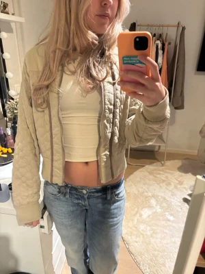 Beige quiltad bomberjacka - Snygg beige bomberjacka med quiltade detaljer och ribbade muddar. Jackan är croppad och har dragkedja framtill. Perfekt för dig som gillar en trendig och avslappnad stil. 